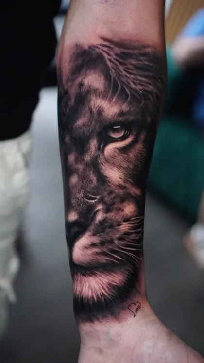Tatuaje realista de león en antebrazo con detalle en pelaje y sombreado por Clayton Goethe